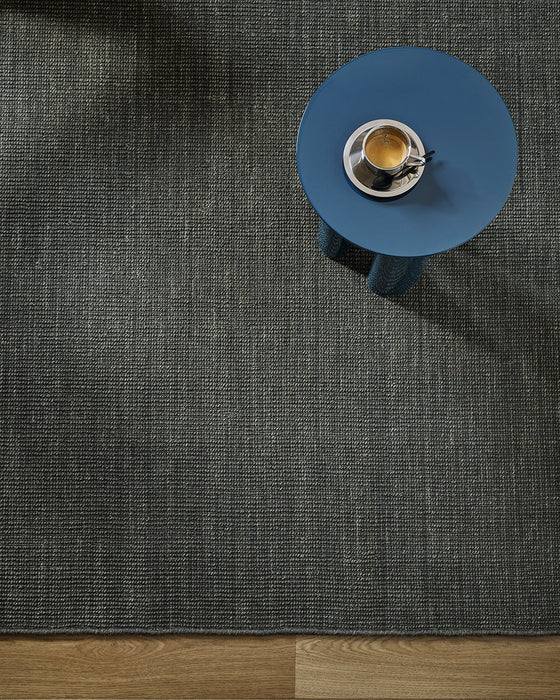 Linden Floor Rug in Petrol, seen from above with a blue side table and a coffee cup
