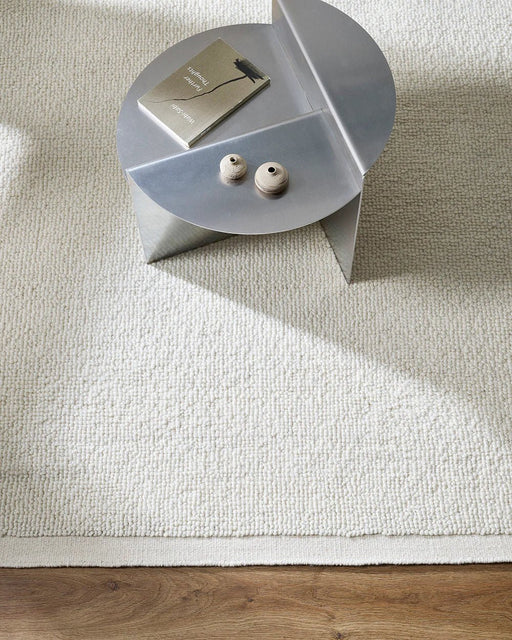 Clifton Floor Rug in Ivory, seen from above with a metal side table, showing the looped pile