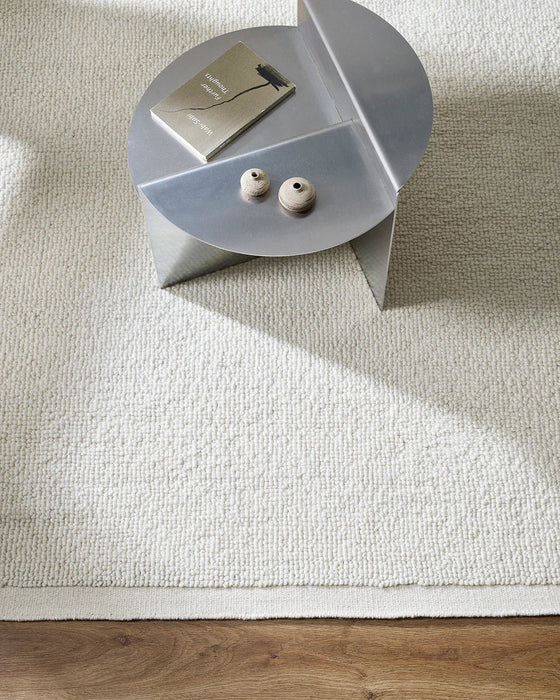 Clifton Floor Rug in Ivory, seen from above with a metal side table, showing the looped pile