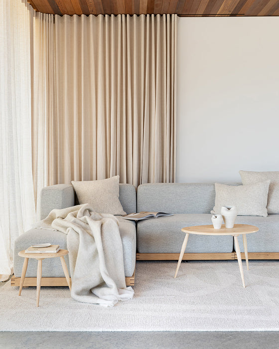 Maya Floor Rug in Oatmeal, in a living room with a pale blue sofa and round timber coffee tables