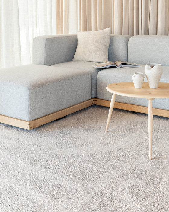 Maya Floor Rug in Oatmeal, under a round timber coffee table beside a pale blue sofa