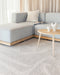 Maya Floor Rug in Oatmeal, under a round timber coffee table beside a pale blue sofa