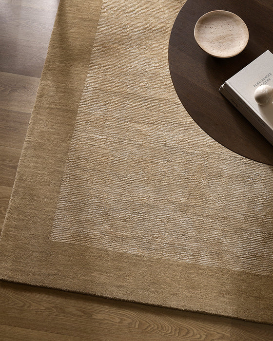Mayfair Floor Rug in Wheat, seen from above under a dark round side table, showing the bordered pile