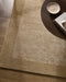 Mayfair Floor Rug in Wheat, seen from above under a dark round side table, showing the bordered pile