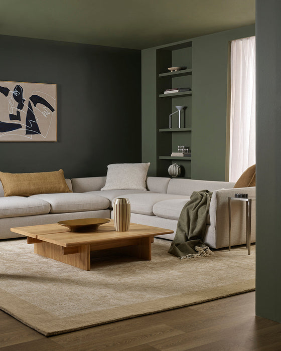 Mayfair Floor Rug in Wheat, in a green living room with a corner sofa, throw and low timber table