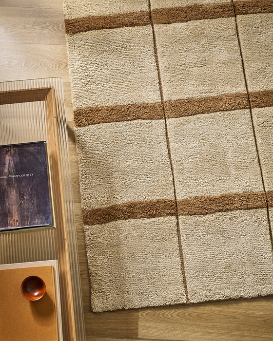 Mesa Floor Rug in Camel, seen from above beside a timber side table, showing the stripe pattern