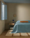 Mesa Floor Rug in Camel, at the foot of a bed with a blue cover in a beige bedroom