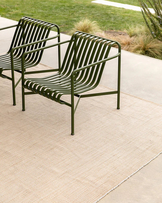 Lonsdale Floor Rug in Almond, on a concrete patio under two green metal outdoor chairs