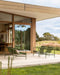 Lonsdale Floor Rug in Almond, on a covered patio with green outdoor furniture beside a garden