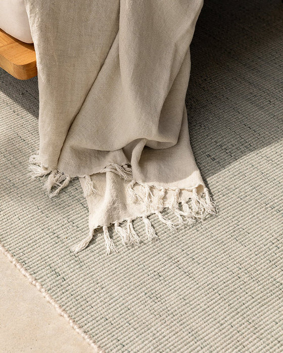Lonsdale Floor Rug in Eucalyptus, close view with a linen throw draped over it, showing the weave