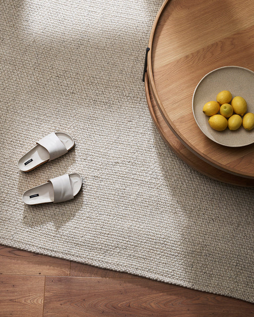 Nebraska Floor Rug in Natural White, seen from above beside a timber tray table and white slides