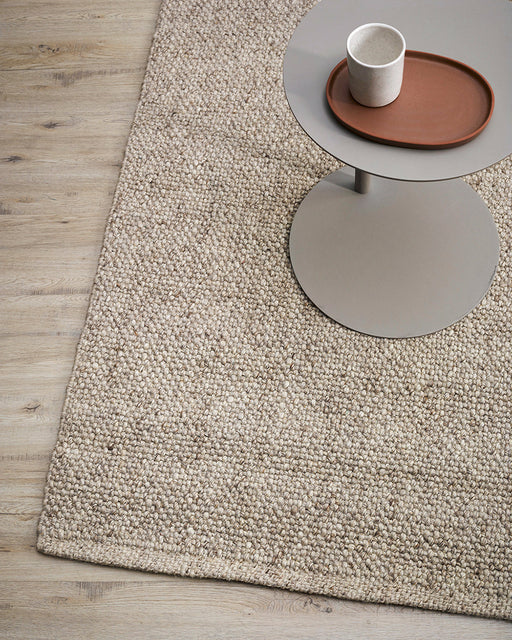 Nebraska Floor Rug in Pebble, close up beside a grey side table, showing the chunky weave