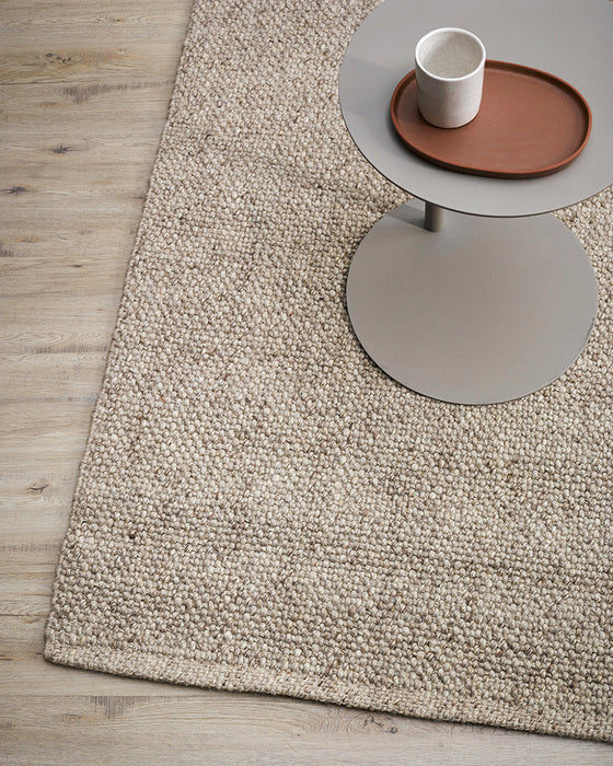 Nebraska Floor Rug in Pebble, close up beside a grey side table, showing the chunky weave