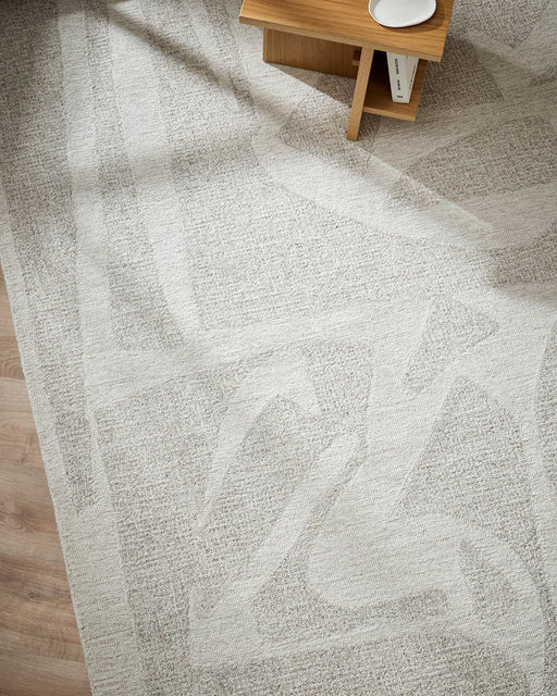 Maya Floor Rug in Oatmeal, seen from above beside a timber side table, showing the abstract pattern