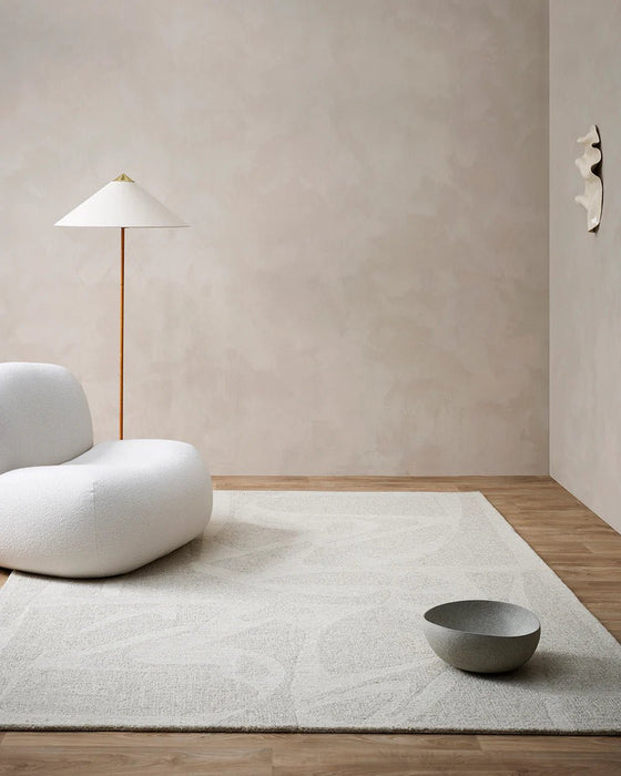 Maya Floor Rug in Oatmeal, in a minimalist room with a cream bouclé chair and floor lamp
