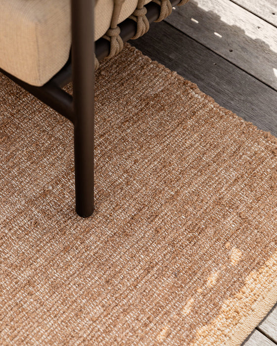 Ormond Floor Rug in Biscotti, close up under an outdoor chair leg on a timber deck, showing the weave