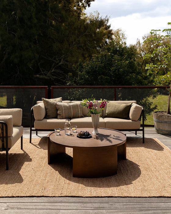 Ormond Floor Rug in Biscotti, on a deck with an outdoor sofa and round timber coffee table