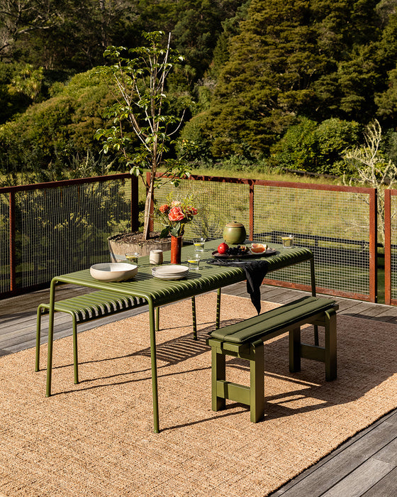Ormond Floor Rug in Biscotti, on a timber deck under a green outdoor dining table and benches