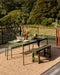 Ormond Floor Rug in Biscotti, on a timber deck under a green outdoor dining table and benches
