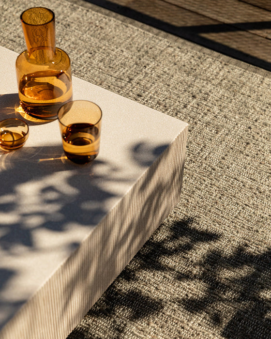 Ormond Floor Rug in Mineral, close up beside a concrete table with amber glasses in dappled light
