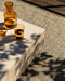 Ormond Floor Rug in Mineral, close up beside a concrete table with amber glasses in dappled light