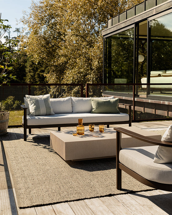Ormond Floor Rug in Mineral, on a timber deck with an outdoor sofa, lounge chair and concrete coffee table