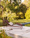 Palm Cove Round Floor Rug in Sand, on a timber deck by a pool with a burgundy sun lounger