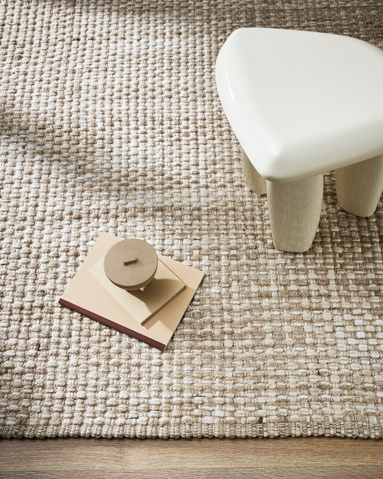 Pelorus Floor Rug in Sand, seen from above beside a white stool, showing the chunky weave