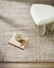 Pelorus Floor Rug in Sand, seen from above beside a white stool, showing the chunky weave