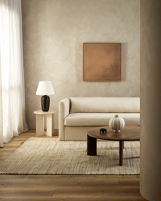 Pelorus Floor Rug in Sand, in a living room with a cream sofa and round dark timber coffee table