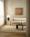 Pelorus Floor Rug in Sand, in a living room with a cream sofa and round dark timber coffee table
