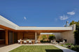 Wide view of a house and lawn under blue sky, with an outdoor dining setting and Blossom armchairs by the stone fireplace wall