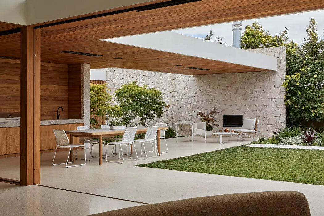 Covered outdoor terrace with a timber ceiling and outdoor dining setting, with Blossom armchairs by the outdoor fireplace