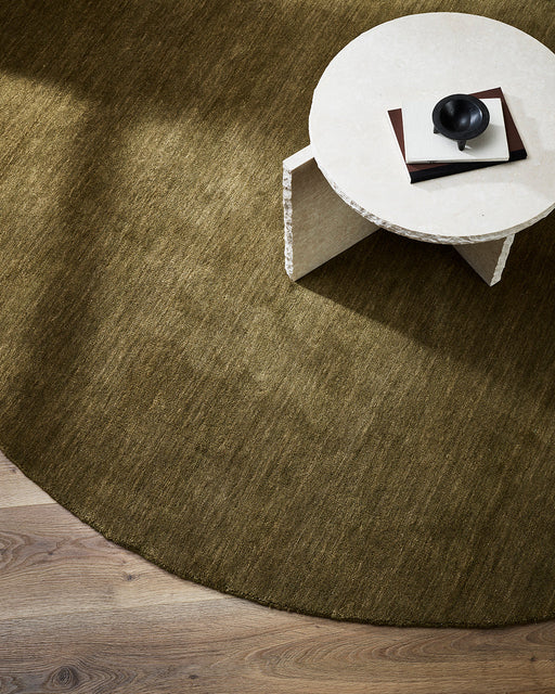 Sandringham Round Floor Rug in Moss, seen from above under a white stone side table, showing the pile