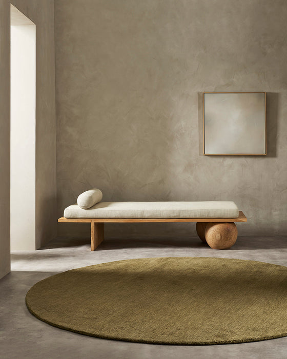 Sandringham Round Floor Rug in Moss, in a minimal room in front of a timber daybed with a bolster