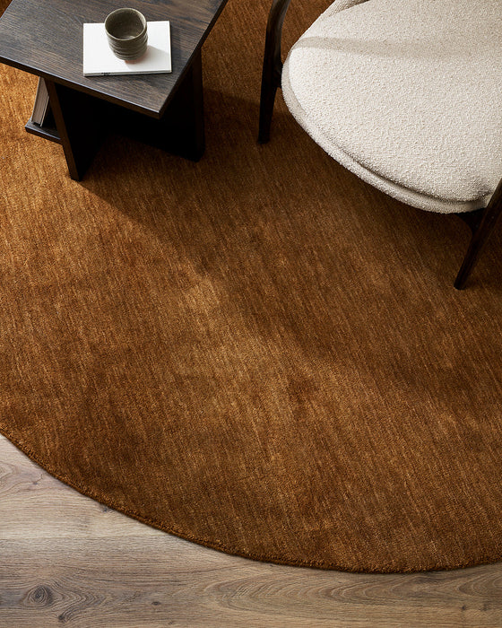 Sandringham Round Floor Rug in Pecan, seen from above beside a dark side table and cream armchair