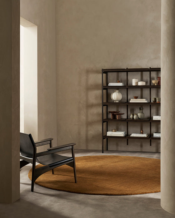 Sandringham Round Floor Rug in Pecan, in a minimal room with a black lounge chair and dark shelving