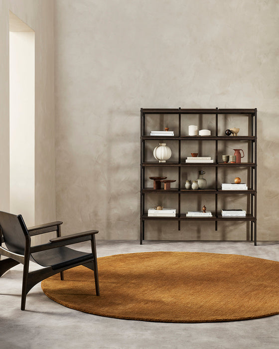 Sandringham Round Floor Rug in Pecan, in a minimal room with a black lounge chair and open black shelving