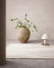 Shoreline Floor Rug in Sand, in a minimal room with a large clay vase and table lamp