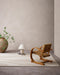 Shoreline Floor Rug in Sand, in a minimal room with a cane armchair, table lamp and large vase