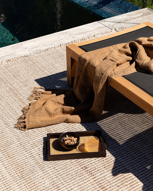 Rhodes Floor Rug in Teak, close up by a pool under a teak lounger with a brown throw