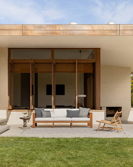 Rhodes Floor Rug in Slate, on a patio outside a modern house with a teak sofa and lounge chair