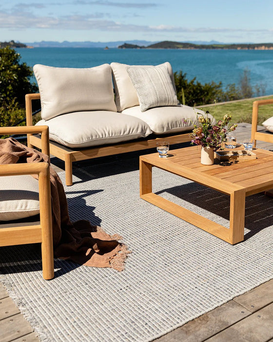 Rhodes Floor Rug in Slate, on a timber deck by the sea with a teak sofa and coffee table