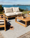 Rhodes Floor Rug in Slate, on a timber deck by the sea with a teak sofa and coffee table