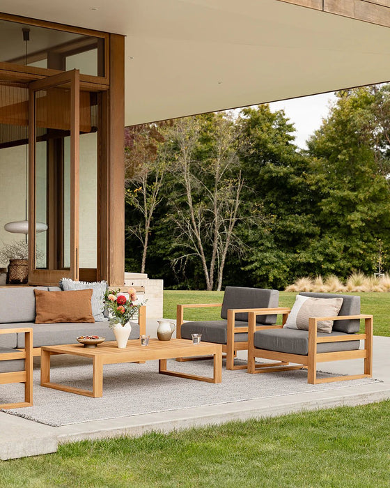 Rhodes Floor Rug in Slate, on a lawn-side patio with teak outdoor sofas and a coffee table