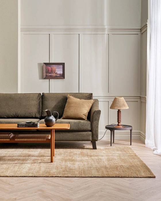 Fairbanks Floor Rug in Sand, in a panelled living room with an olive sofa and timber coffee table
