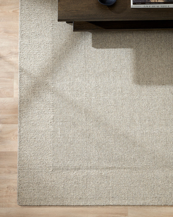 Vermont Floor Rug in Driftwood, seen from above under a dark timber coffee table, showing the bordered weave